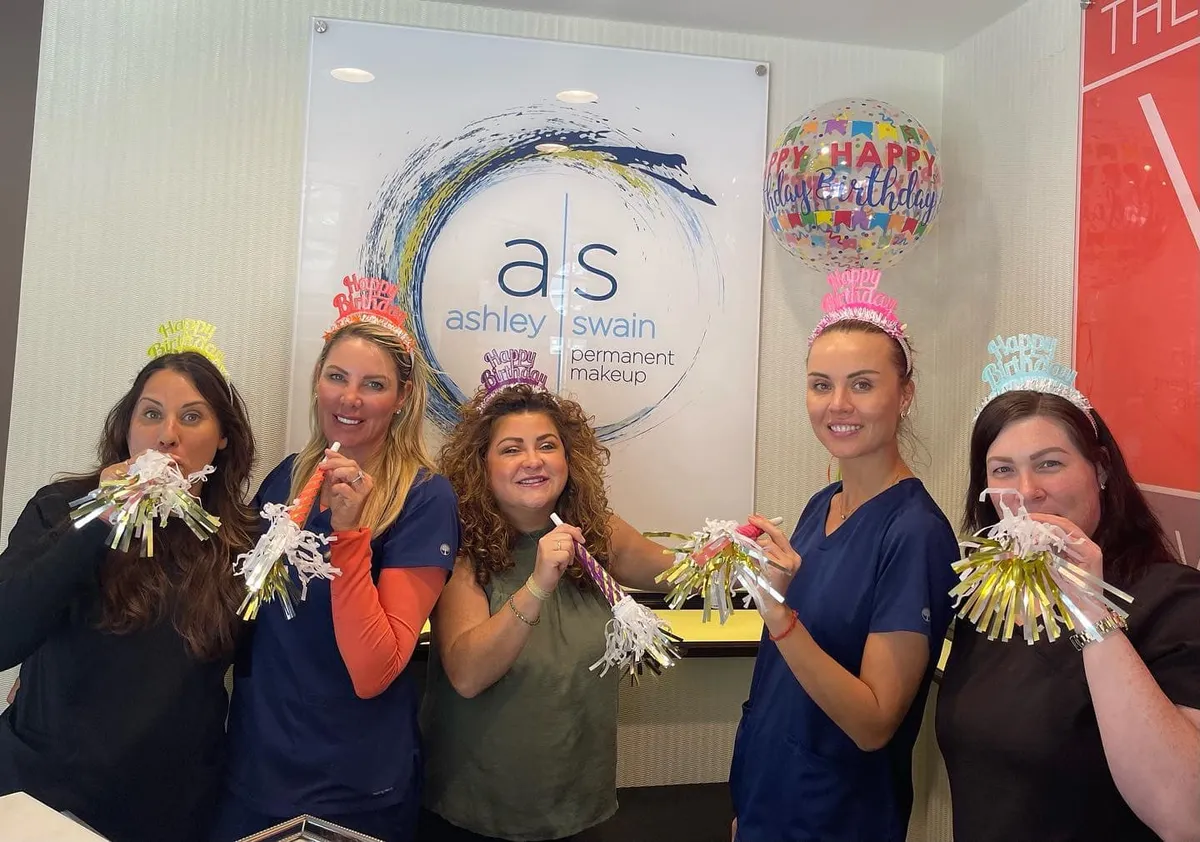 The Ashley Swain team smiling together in front of the studio sign
